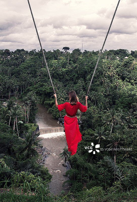 身穿红色连衣裙的女人在巴厘岛丛林中的秋千上飞舞图片素材