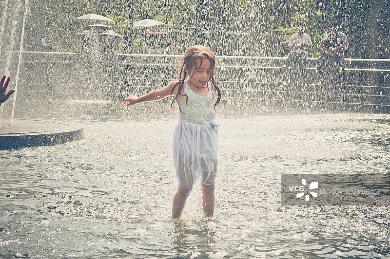 在公园喷泉的水中跳跃的年轻女孩图片素材