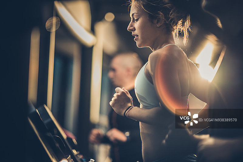 在健身俱乐部运动训练期间在跑步机上跑步的健壮女人图片素材