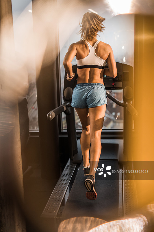在健身房跑步机上进行心血管训练的女子背影图片素材