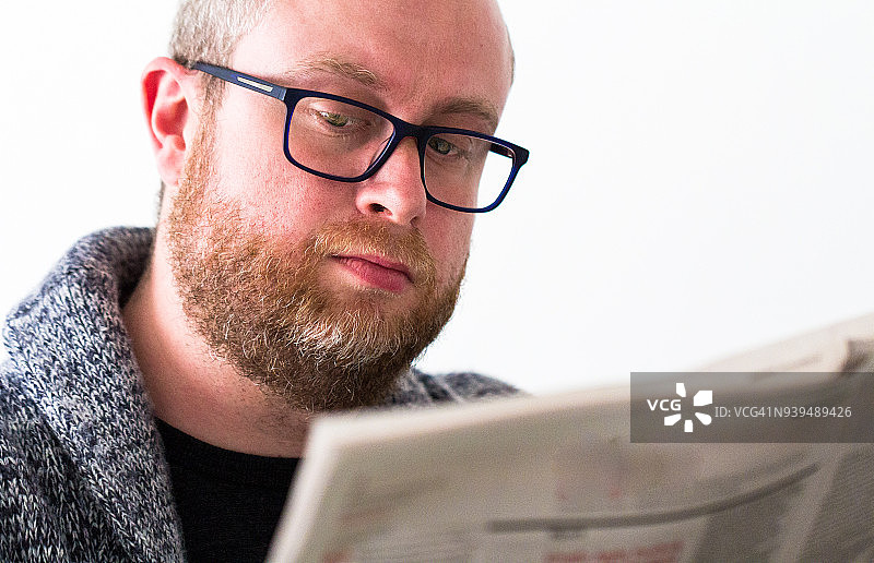 戴眼镜留着胡须的年轻男人阅读报纸特写图片素材