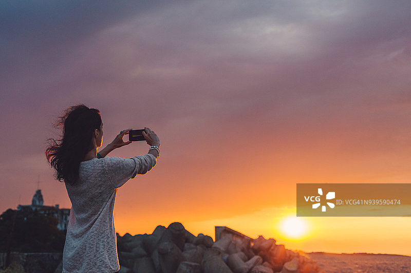在海滩上拍摄日落的女人图片素材