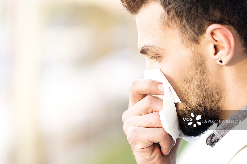 英俊男人在散景背景下擤鼻子的侧面照图片素材