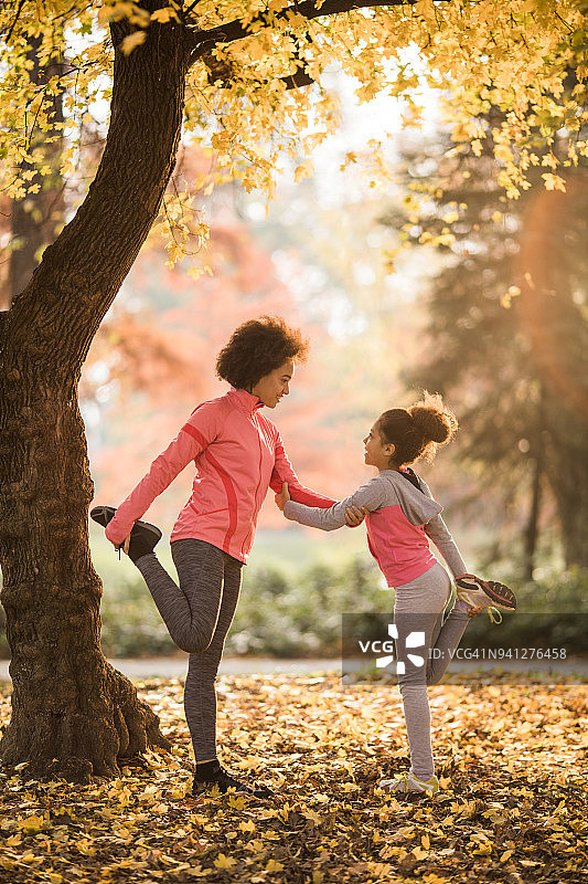 非裔美国母亲和女儿在秋日里合作伸展双腿图片素材