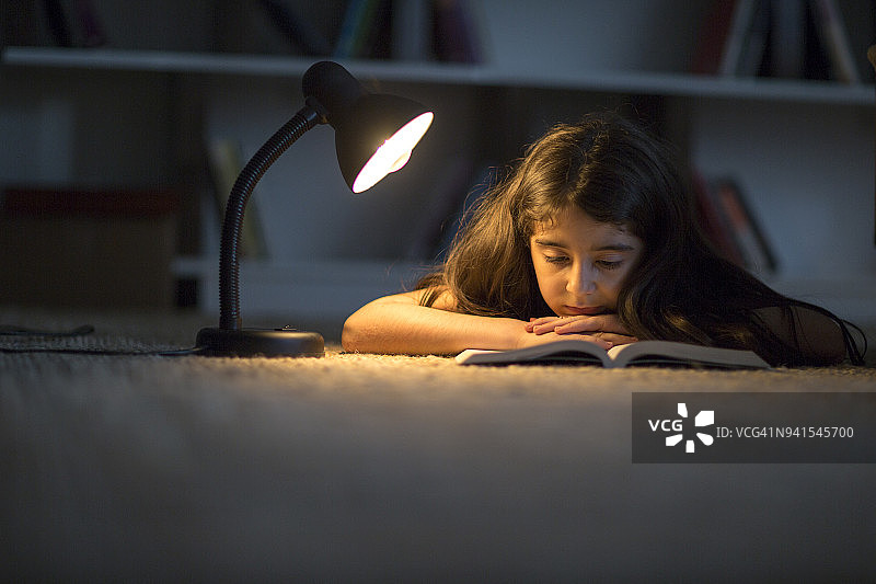 儿童在夜晚的黑暗中和玩具熊一起读书图片素材