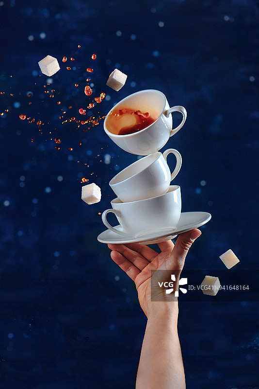 手指尖上平衡的瓷杯和茶托，深色背景上的咖啡飞溅的动态饮品摄影图片素材