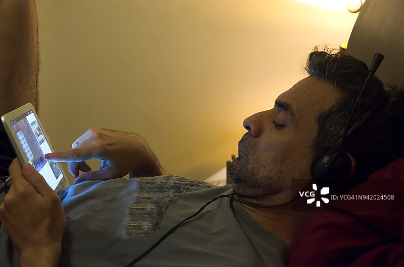 一位中年男子在床上用平板电脑娱乐图片素材