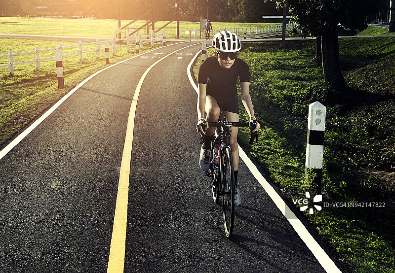 戴头盔的亚洲健康女孩在自行车道上骑行锻炼图片素材