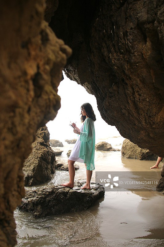 年轻的波西米亚时尚女性站在加利福尼亚州马里布El Matador海滩的洞穴中，阳光明媚图片素材