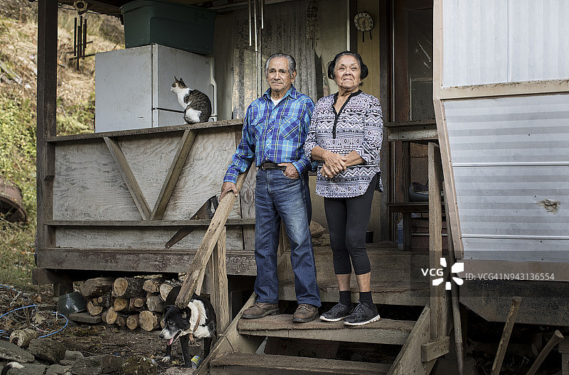 一对已婚的美国原住民老年夫妇在简朴住宅的前廊上，有猫、狗和木柴图片素材