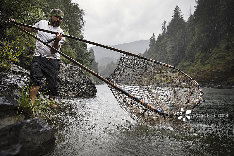 年轻的北美洲原住民男子站在浅河中捕捞红眼鲑鱼图片素材