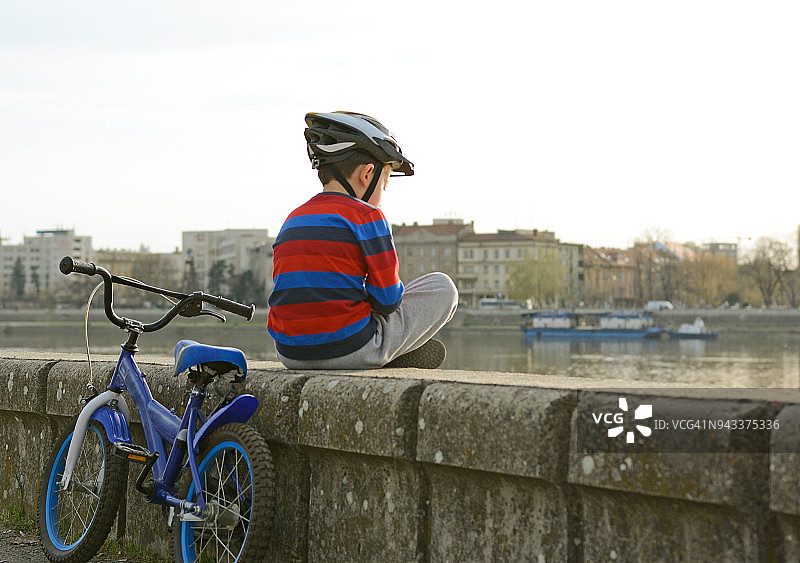 小男孩在河边骑行后孤独地休息图片素材