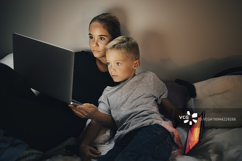男孩在家中靠在床上玩平板电脑，妹妹使用笔记本电脑图片素材