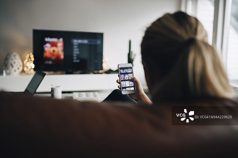 在家看电视时使用智能手机APP的少女背影图片素材