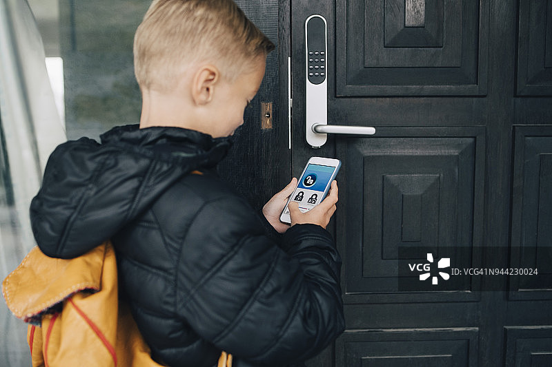 男孩用智能手机App开门回家背影图片素材