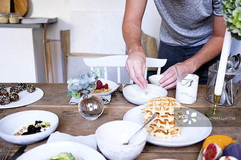 男子在木桌上用酸奶装饰盘子的身体中部照片图片素材