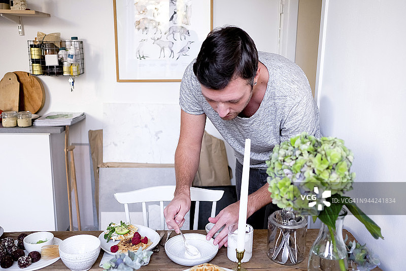 男人在家中桌子的盘子里涂抹酸奶图片素材