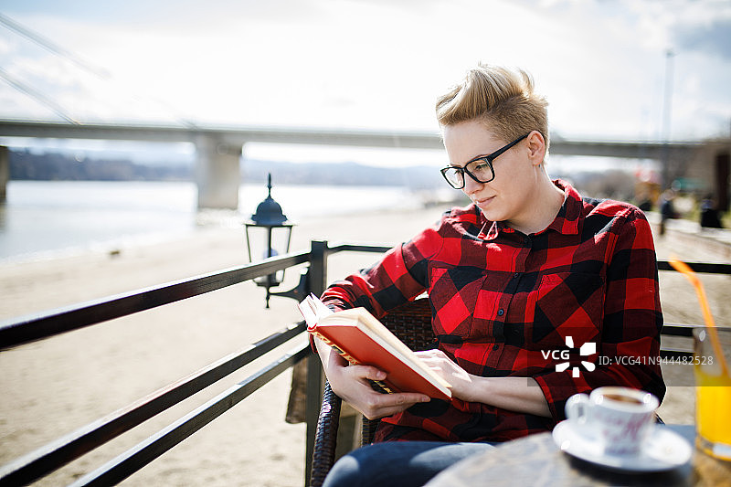 在河岸咖啡馆里看书的年轻漂亮女人图片素材