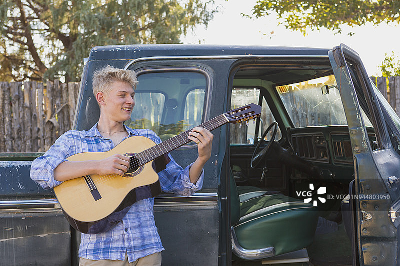 青少年男孩弹吉他，靠在皮卡车上图片素材