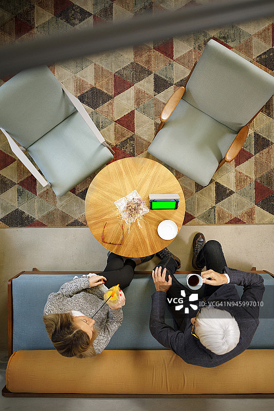 老年夫妇在复古酒店喝咖啡聊天，使用平板电脑和智能手机浏览互联网图片素材