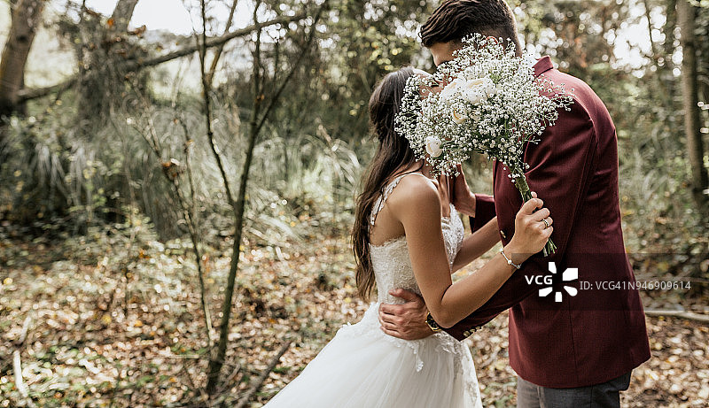 森林中亲吻的新人，手捧鲜花，面部不可见图片素材