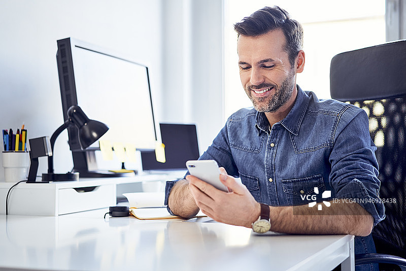 微笑的男人在办公室的办公桌旁使用手机图片素材