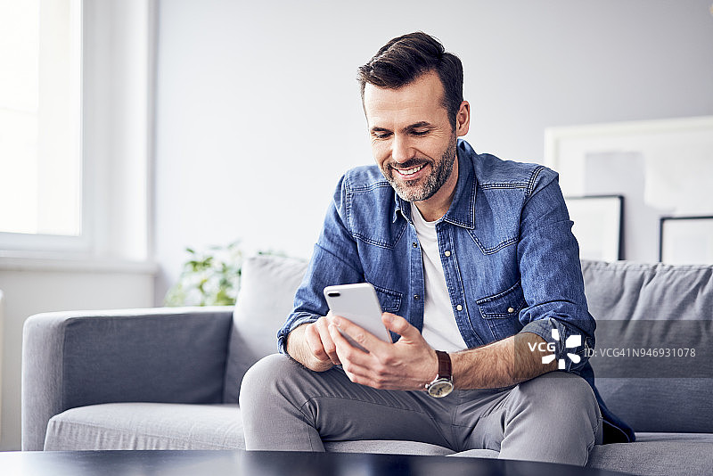 微笑的男人坐在沙发上使用手机图片素材