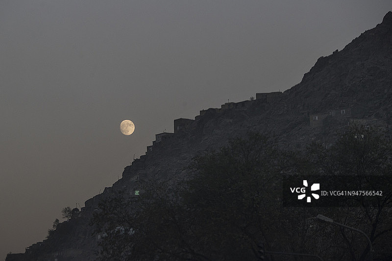 喀布尔山坡上的房屋上空的月亮图片素材