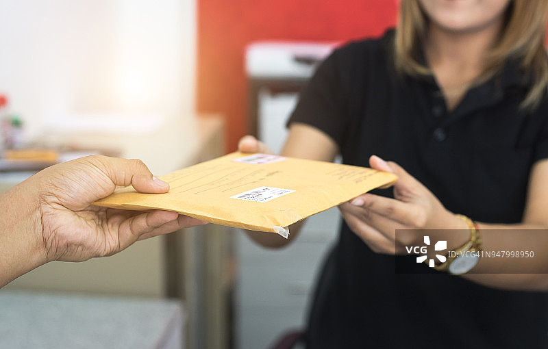 男人在寄信前将邮件信封发送给邮局的女人图片素材