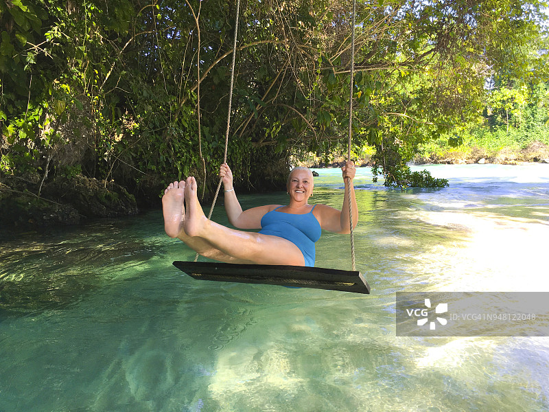 快乐的老年妇女在牙买加热带河流上的秋千上图片素材
