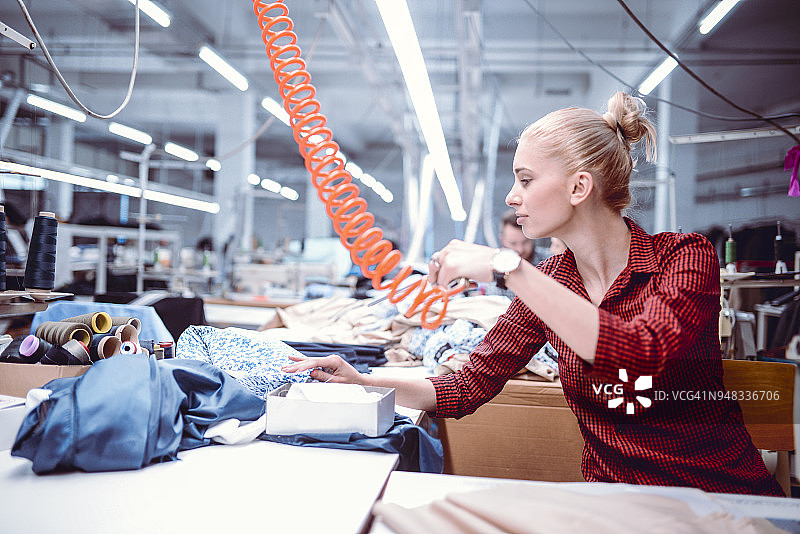 年轻的纺织工吹掉材料上的缝纫线图片素材