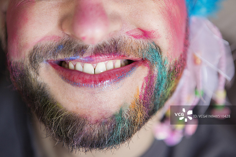 微笑的男人涂着口红，化着妆，胡子上涂着彩色粉笔图片素材