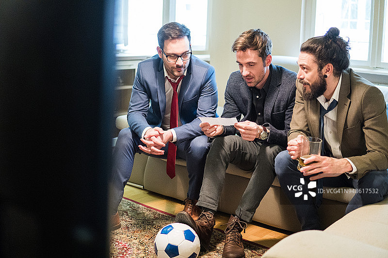 快乐的三名男性足球支持者看着博彩单图片素材