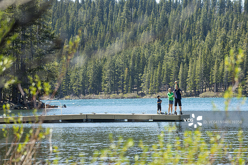 爸爸、妈妈和两个儿子在湖边码头露营，进行飞蝇钓鱼图片素材