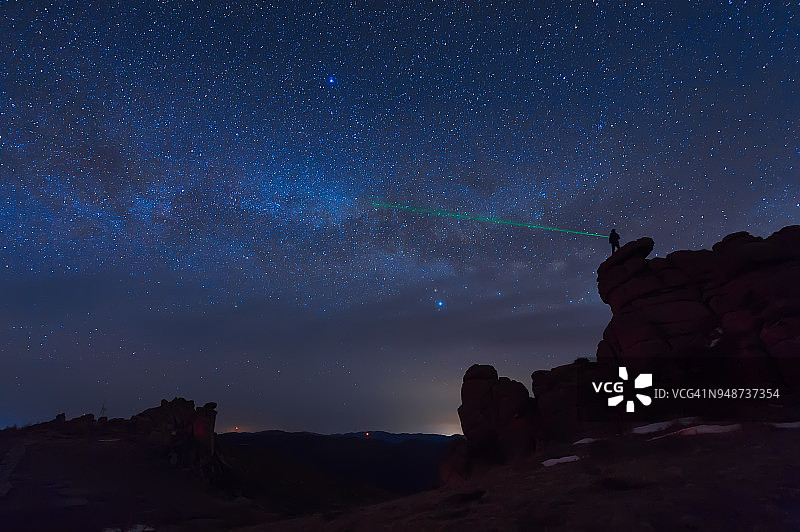一个人站在户外，用绿色激光笔指向银河系中的一颗明亮的星星图片素材