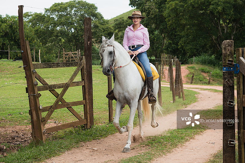 在农场大门上骑马的牛仔女郎图片素材