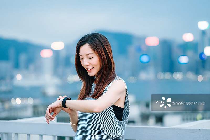 在香港城市天际线下使用智能手表的年轻女子图片素材