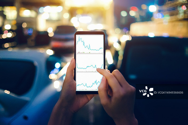 人手在停车场查看手机上的金融交易数据，同时走向汽车图片素材