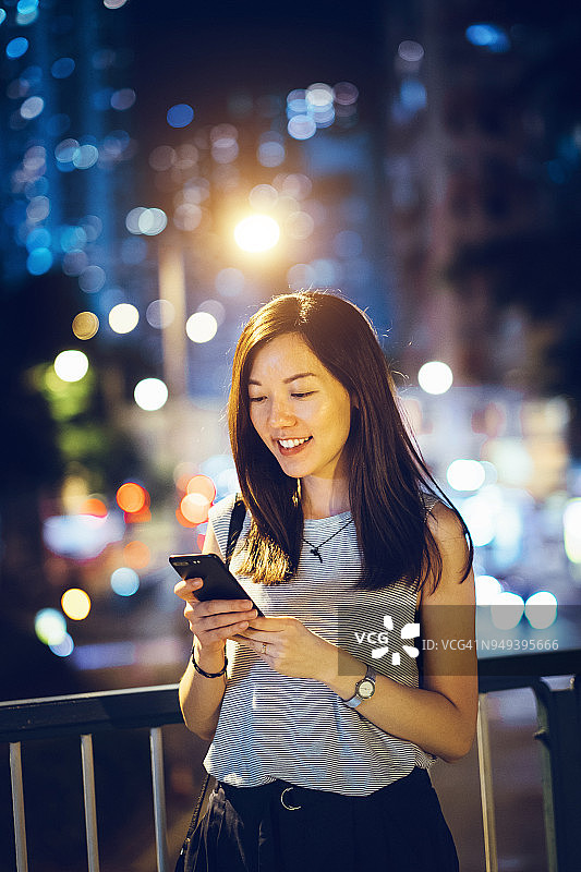 在市中心夜晚的街道上用智能手机发短信的美丽女人图片素材