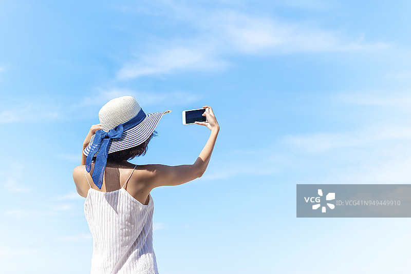 在海滩上快乐的暑假旅行：女士在蓝天下自拍图片素材