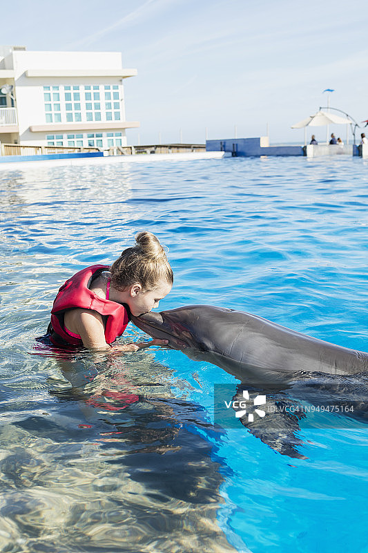 小女孩站在水中抚摸和亲吻海豚图片素材