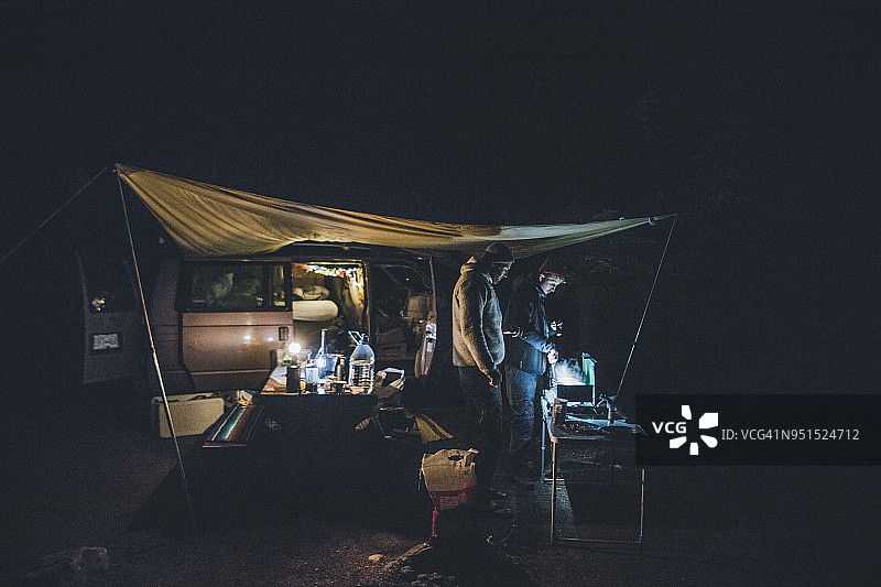 加拿大不列颠哥伦比亚省，两名男子在夜间的小型货车上用防水布做饭图片素材