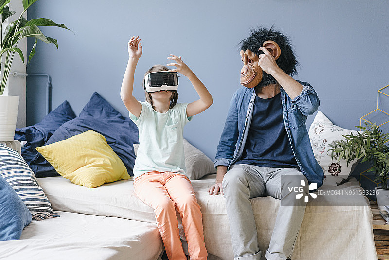 父亲戴着猴子面具看着在家戴VR眼镜的儿子图片素材