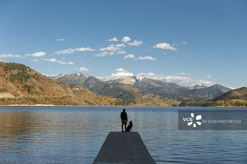男子与德国牧羊犬站在美国爱达荷州湖边码头欣赏风景的剪影图片素材