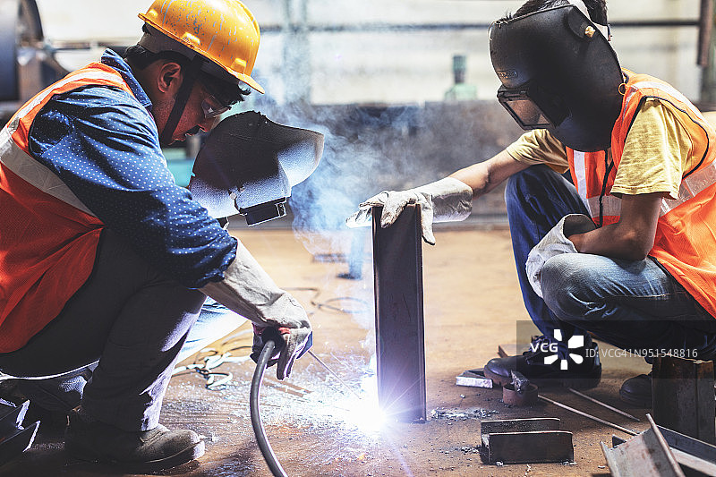 当老员工焊接另一块时，年轻员工稳稳地握住金属图片素材