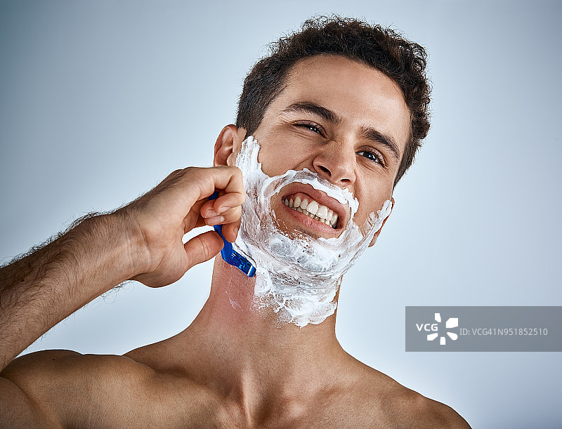 年轻男人刮胡子时不小心刮伤自己，面露痛苦图片素材