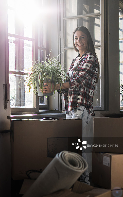 用盆栽植物装饰新公寓的年轻快乐的女人图片素材