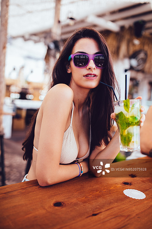 戴比基尼和太阳镜，喝鸡尾酒的年轻时尚女人图片素材