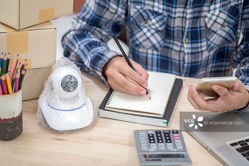 年轻的创业小企业主在工作场所将监控摄像头装箱。自由职业者在家准备产品包装。在线销售。图片素材