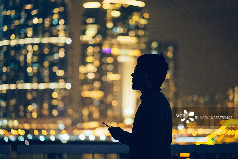 夜晚城市天际线背景下使用手机的男人轮廓图片素材
